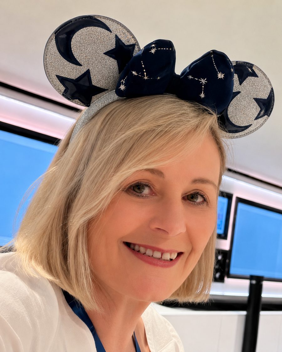 Connie Buck smiling, wearing navy Mickey ears embroidered with silver stars and constellations